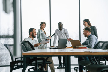 Against big panoramic windows. Team of office workers are together indoors
