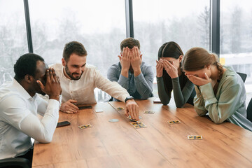 Covering eyes with hands. Playing card game. Team of office workers are together indoors