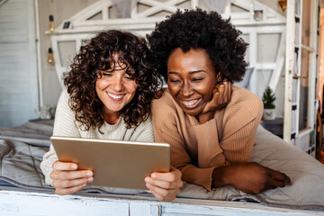 LGBT Multiethnic diverse homosexual lesbian couple spending happy time together with digital tablet.