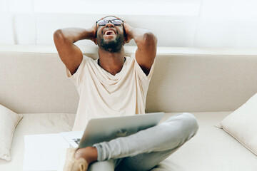 Smiling African American Freelancer Working from Home on a Sofa with Laptop A happy young African...