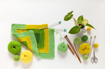Top view of hand knitting square pattern using 10-stitch method from yarn of green and yellow wool on white backgroung. Spring needlework concept. Flat lay, copy space, close-up, mock up