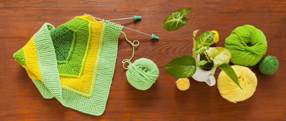 Beautiful composition with hand knitting square pattern using 10-stitch method from yarn of green and yellow wool on wooden table. spring needlework. Flat lay, top view, close-up, mock up