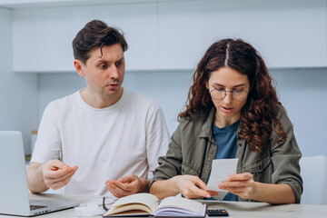 A concerned man and a focused woman sit together, budgeting with receipts and a calculator, highlighting the importance of financial planning. A married couple forms a budget, considers expenses for a