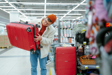 Man Inspecting Red Suitcase in Shopping Aisle for Travel Accessories. A shopper carefully examines a bright red suitcase in the store, perhaps planning for an upcoming travel adventure