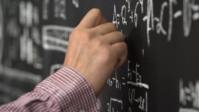  A male hand writing on blackboard. Man's hand writing with chalk on board. Close view teacher's hand writing on blackboard in classroom. Professor teaching math on blackboard. 