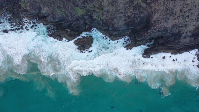 Ocean waves crash against the rocks, creating white foam. Top view from a drone on the sea surface.
