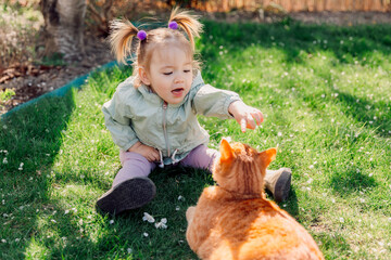 Child girl playing with ginger cat in spring garden