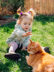 Child girl with ginger cat on lawn in spring backyard garden
