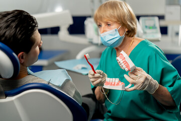 in a dental clinic a dentist shows a patient how to brush his teeth correctly - obrazy, fototapety, plakaty
