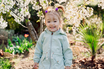 Smiling cute child girl in jacket in blooming garden. - 781299007