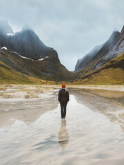 Alone with nature - traveler woman walking on flooded Horseid beach in Norway, traveling solo outdoor healthy lifestyle active vacations tour in Lofoten islands mountains water reflection, solitude - 781302032