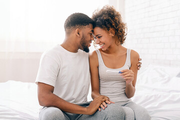 Happy couple holding positive pregnancy test on bed