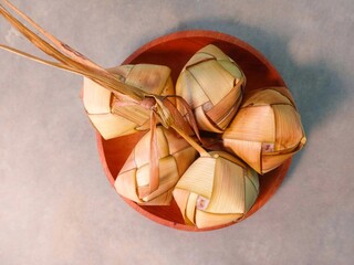 ketupat, traditional Indonesian food. made from rice put into woven young coconut leaves and then boiled. ketupat served on a wooden plate on a gray background. Flat lay