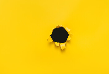 Torn hole in yellow paper with black empty background. Copy space, mockup. Place for text or logo.