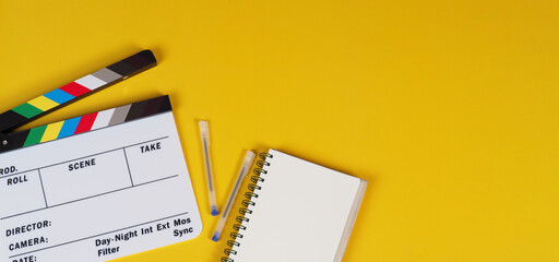 Clapper board with notebook and pens on yellow background.