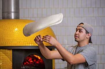 Skilled chef preparing dough for pizza rolling with hands and throwing up. The chef tosses the pizza dough into the air. Hands of a male chef with thin round pizza dough in the kitchen