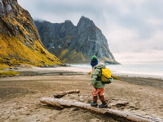 Active travel vacations in Norway - child hiking on Kvalvika beach in Lofoten islands adventure family tour outdoor active healthy lifestyle 4 years old kid with backpack exploring scandinavian nature - 781311069