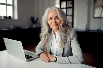 A portrait of a middle-aged business woman sitting at the table with laptop in her office