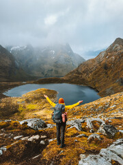 Traveler woman hiking with backpack in Norway travel in Lofoten islands outdoor healthy lifestyle active autumn vacations adventure, girl happy raised hands enjoying lake and foggy mountains nature