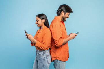 Young couple engrossed in smartphones on blue background