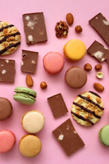 Pastel macarons, almond chocolate, peanut butter cookies and various nuts on bright pink background. Top view.