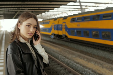 Portrait of a young woman talking on mobile phone waiting for a train at a station  - 781317271