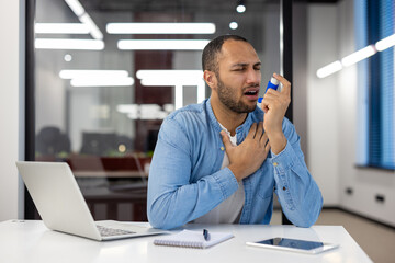 Indian man using an inhaler for asthma in the office