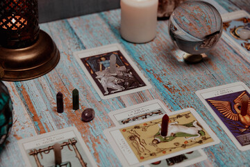 A dimly lit scene showing a spread of tarot cards, alongside crystals, candles, and a crystal ball...