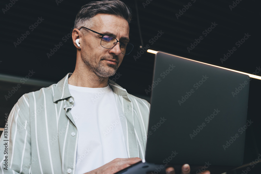Poster caucasian businessman in glasses and electronic earbuds browsing website with marketing webinar, ski