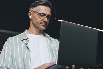 Caucasian businessman in glasses and electronic earbuds browsing website with marketing webinar,...