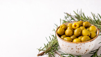 Marinated green olives in a bowl on white background. Copy space