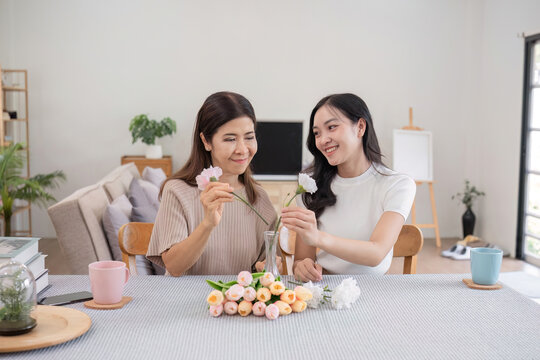 Middle-aged daughter happily arranges flowers with her mother at home Free time activities that are done together as a family