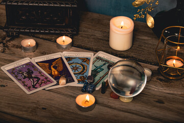 Close-up of a tarot card arrangement with a crystal ball and flickering candles on an aged wooden...