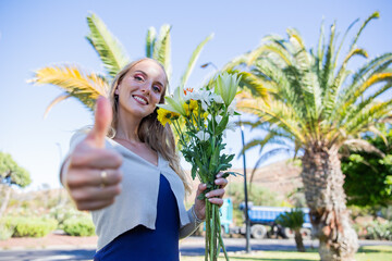 A young beautiful woman is holding a bouquet of flowers and giving a thumbs up