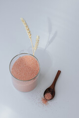 A glass jar with pink Himalayan salt stands on a white background with two ears of wheat casting a...