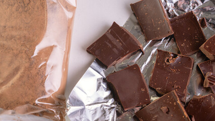 Chocolate broken into chunks and package of cocoa powder top view on white table, chocolate...
