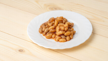 Beans on a white plate on a wooden background.