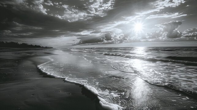 A black and white photo of a beach with the sun shining on the water