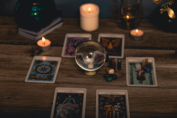 Close-up of a tarot card arrangement with a crystal ball and flickering candles on an aged wooden surface.