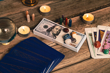 A tarot spread with The Fool card, hundred-dollar bills, and various crystals on a rustic wooden...