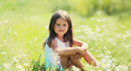 Naklejka na ściany i meble Happy little girl child sitting on grass in sunny summer park
