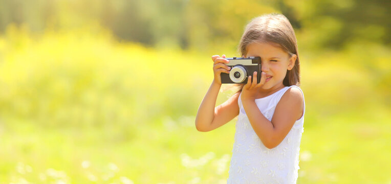 Child with film camera taking picture outdoors on sunny summer day