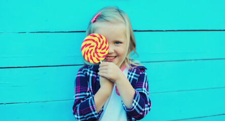 Portrait of happy cheerful smiling child with sweet lollipop on stick on blue background