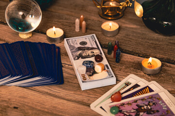 A tarot spread with The Fool card, hundred-dollar bills, and various crystals on a rustic wooden...