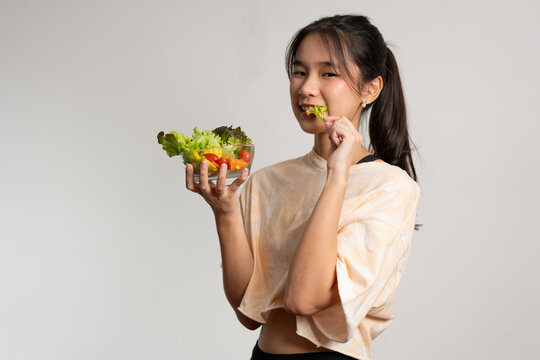 Portrait of a happy playful Asian girl eating fresh salad from a glass bowl after workout at home. Young lady Enjoying Healthy Nutrition And Organic Food, Having Vegetarian Meal
