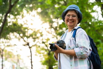 Portrait of Asian mature woman holding a camera and backpack behind her back, an Asia active senior...