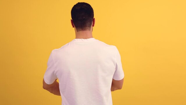  Young man standing on yellow background standing backwards looking away with arms crossed