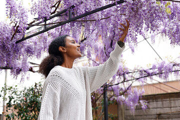 An astonished African American woman is touching a gorgeous purple wisteria flower in the garden...