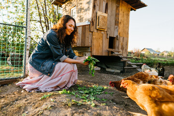 Happy middle aged woman on a private farm feeding chickens. Joyful farmer woman caring for her bird in her backyard in a rustic style, demonstrating an eco-friendly lifestyle. Sustainable lifestyle