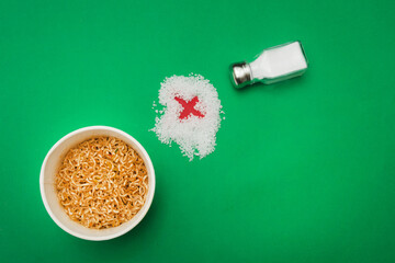 Wok noodles, salt shaker and salt cross against green background. Please add salt to your food in moderation. Over-salted food is harmful to health. Flat lay